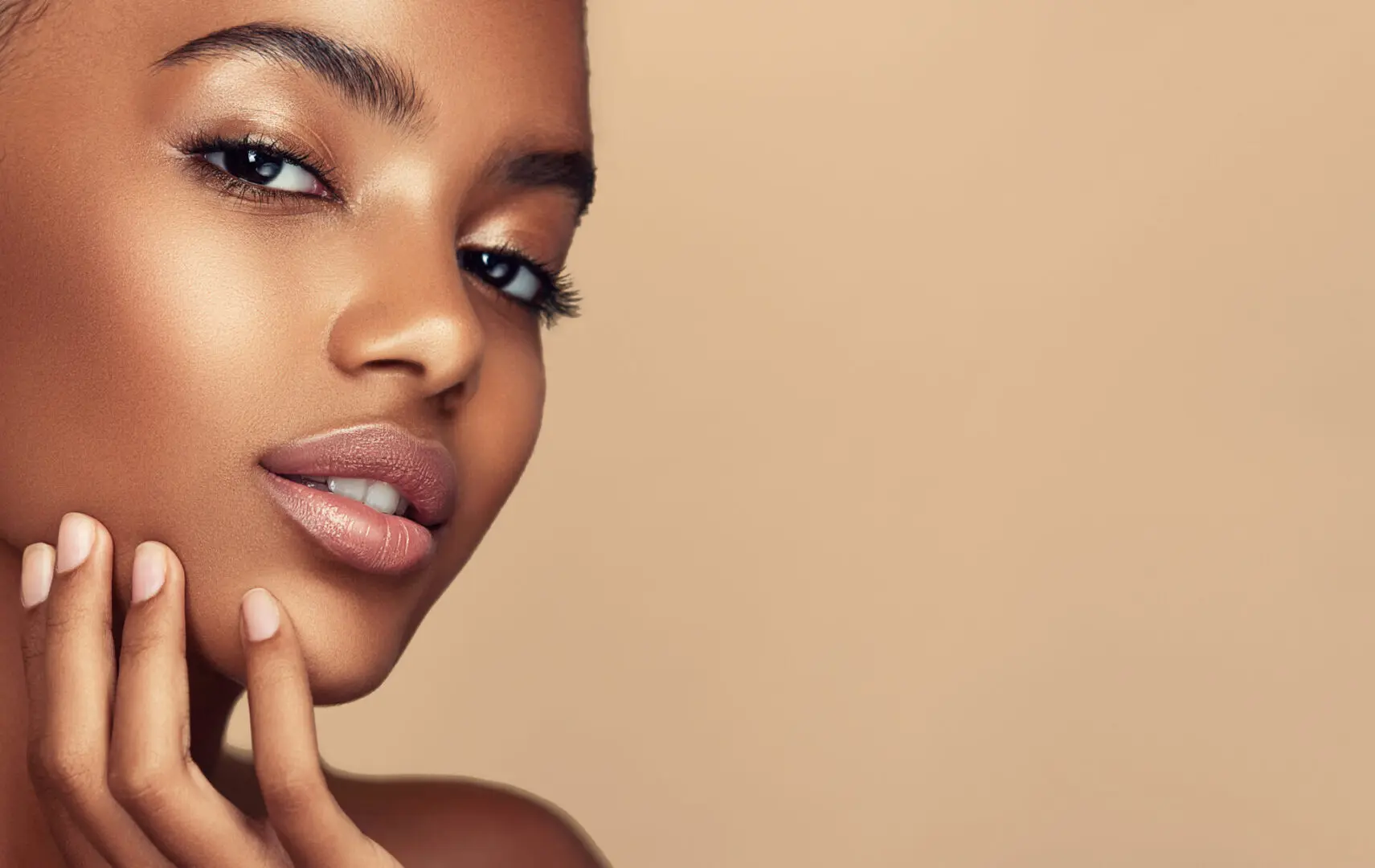 Pearl teeth behind ripe well shaped rose lips and soft, kind look of black eyes. Close up portrait of young, beautiful model with with vibrant, melanin-rich skin tone. Beauty, makeup and cosmetology.